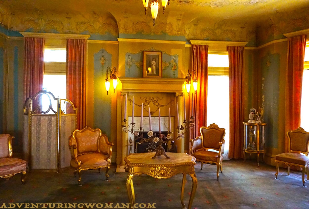 The Overholser mansion front parlor is a feminine room and clearly Anna Overholser's domain. Rose-colored upholstery and draperies, lots of gold gilt, and flower motifs on the fireplace and the painted wallpaper characterize the room.