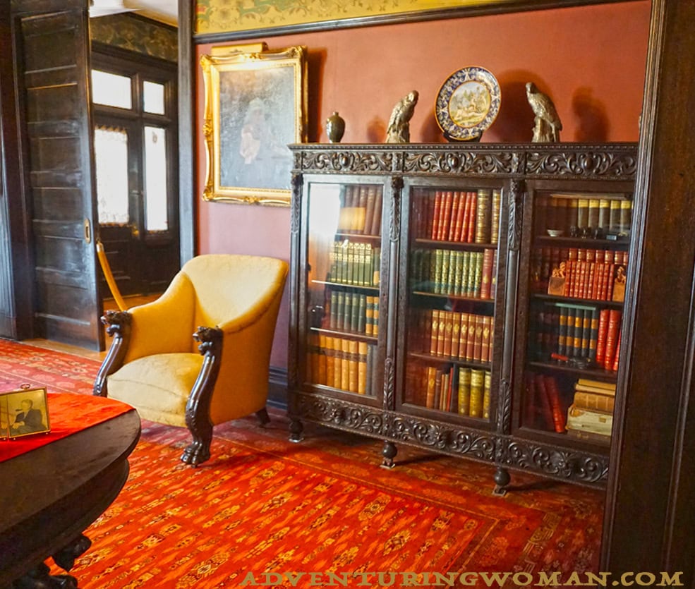 An elaborately carved bookcase in the library holds colorful leather-bound books. A deep armchair is one of the comfortable seats in this cozy room.