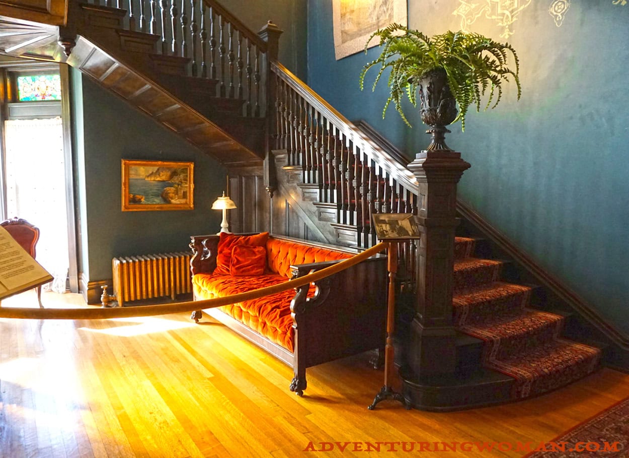 The front entryway and grand stairway of the Overholser mansion in Oklahoma City. There is a dedicated fireplace across from the couch and additional seating in the turret area.