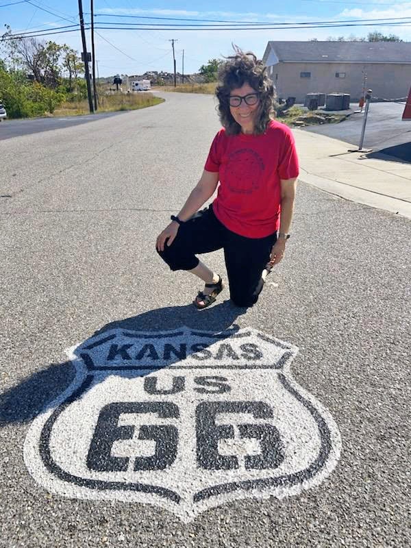 Cynthia, the Adventuring Woman, poses on the highway with the US Route 66 Kansas logo. Hope no cars come!