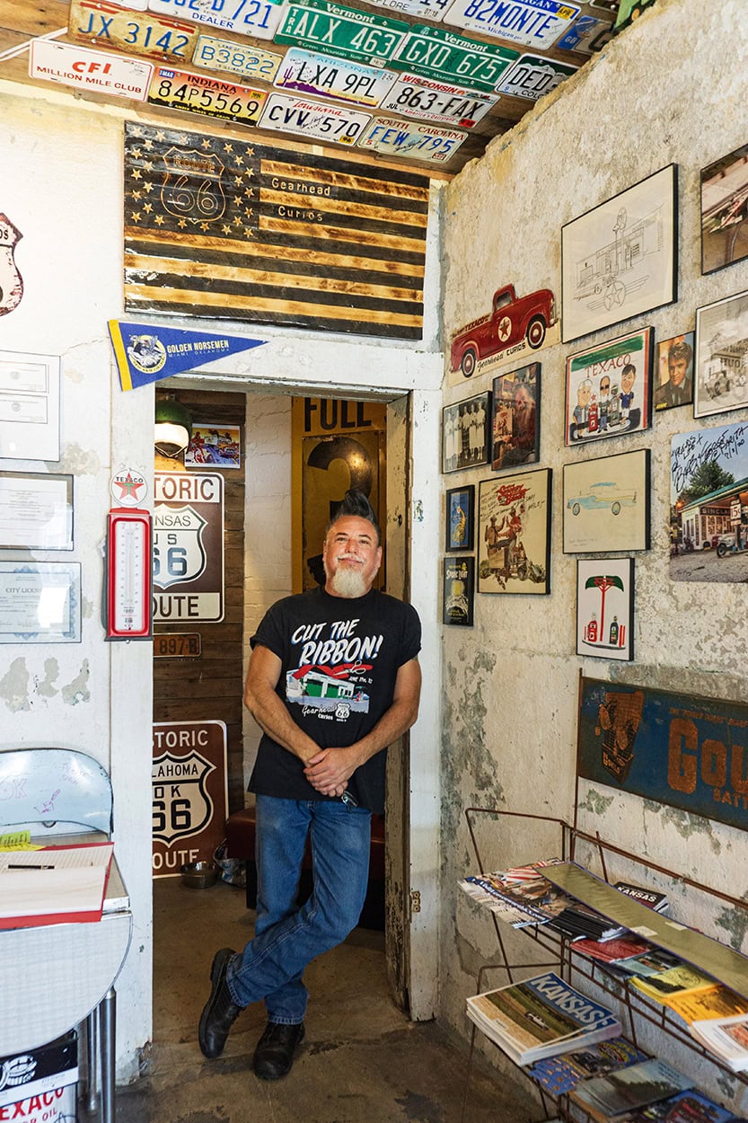 Shows Aaron, the proprietor of Gearhead Curios, inside his restored gas station and must-see tourist attraction on US Route 66 in Kansas. The ceiling is covered with license plated from all over the US.